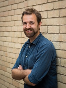 author standing against a wall with his hands folded over his chest